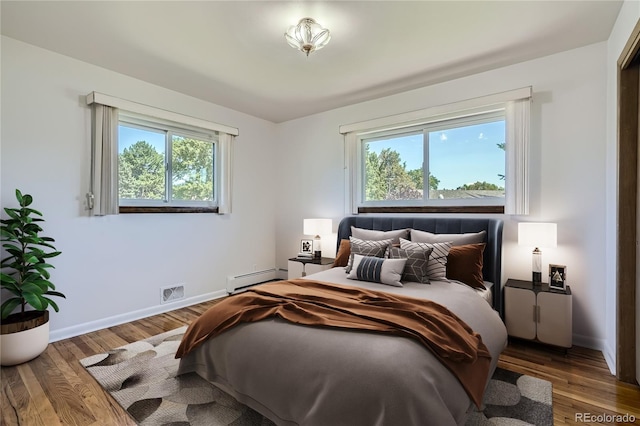 bedroom featuring multiple windows, baseboard heating, and hardwood / wood-style flooring