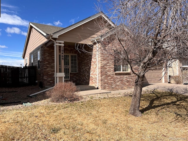 view of side of home featuring brick siding, fence, a yard, a garage, and driveway