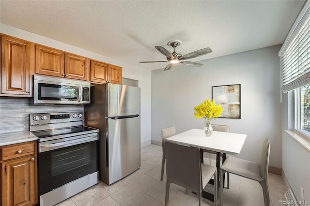 kitchen with a textured ceiling, a kitchen breakfast bar, ceiling fan, stainless steel appliances, and light tile patterned floors