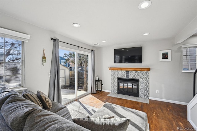 living area featuring a tiled fireplace, wood finished floors, visible vents, and baseboards