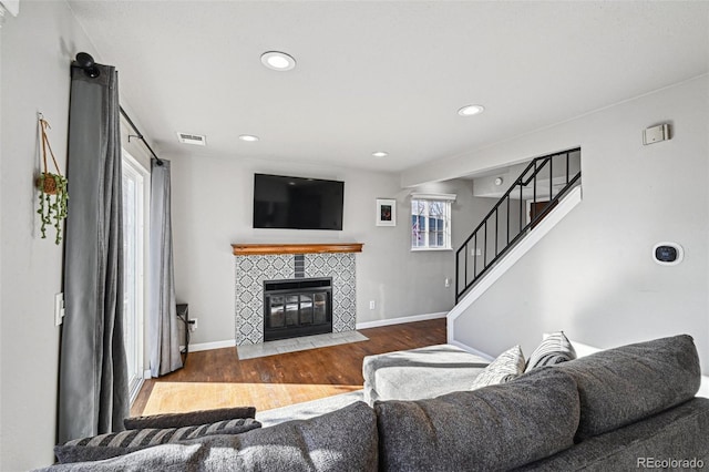 living room with a fireplace, wood finished floors, visible vents, baseboards, and stairway