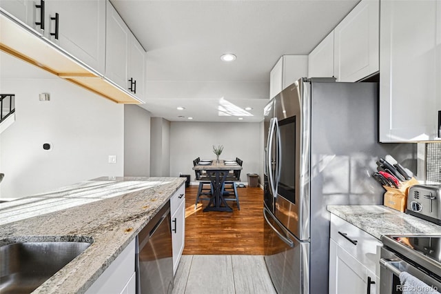 kitchen with light stone countertops, white cabinetry, stainless steel dishwasher, and wood finished floors