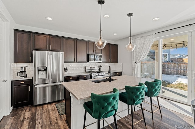 kitchen featuring a kitchen island with sink, dark brown cabinets, stainless steel appliances, a kitchen bar, and decorative light fixtures