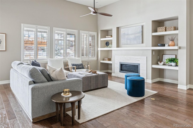 living room with built in shelves, ceiling fan, and wood-type flooring