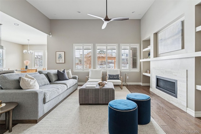 living room with built in features, hardwood / wood-style flooring, ceiling fan with notable chandelier, and a stone fireplace