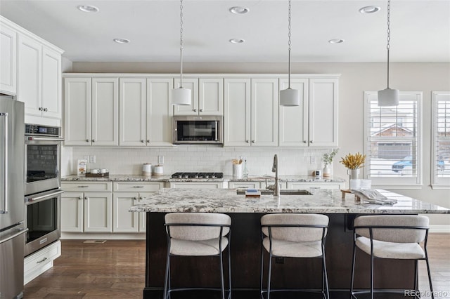 kitchen with decorative light fixtures, white cabinetry, appliances with stainless steel finishes, and a center island with sink