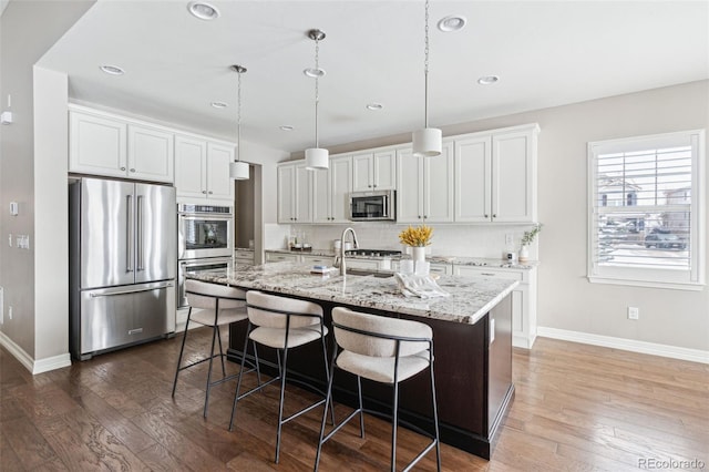 kitchen with pendant lighting, appliances with stainless steel finishes, sink, white cabinetry, and a kitchen island with sink