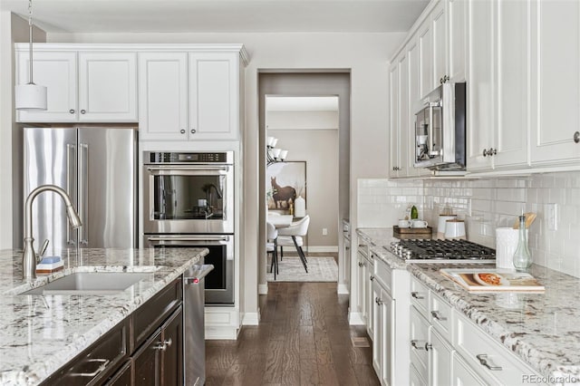 kitchen with hanging light fixtures, white cabinets, sink, stainless steel appliances, and light stone counters