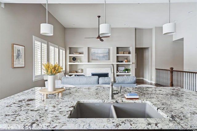 kitchen featuring sink, built in shelves, light stone counters, and decorative light fixtures