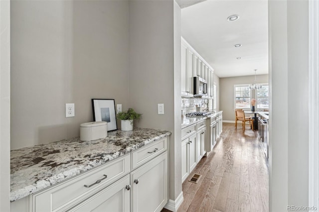 kitchen with white cabinetry, stainless steel appliances, decorative backsplash, light hardwood / wood-style floors, and hanging light fixtures