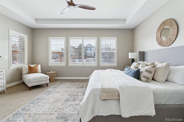 carpeted bedroom with ceiling fan, multiple windows, and a tray ceiling