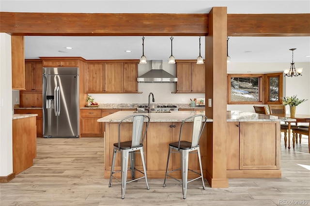 kitchen featuring light stone countertops, wall chimney range hood, stainless steel appliances, and decorative light fixtures