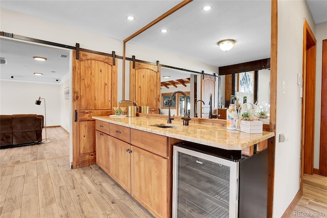 kitchen with a barn door, beverage cooler, a sink, light wood-style floors, and open floor plan