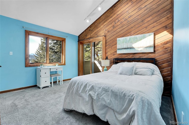 bedroom featuring lofted ceiling, rail lighting, light colored carpet, wood walls, and baseboards