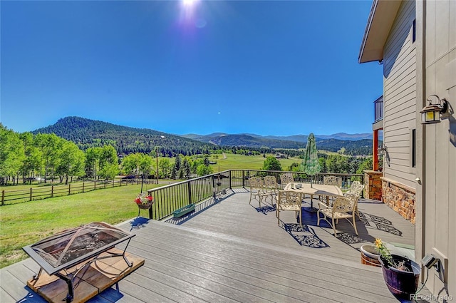 wooden deck featuring outdoor dining area, a yard, an outdoor fire pit, a mountain view, and a fenced backyard