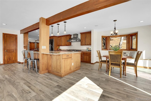 kitchen with a peninsula, wall chimney range hood, hanging light fixtures, and light wood-style floors