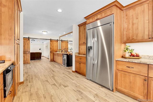 kitchen featuring light stone counters, a barn door, light wood-style floors, beverage cooler, and stainless steel fridge