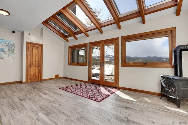 entrance foyer with french doors, a wood stove, a mountain view, light wood-type flooring, and vaulted ceiling with skylight