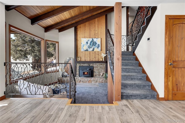 staircase with lofted ceiling with beams, wood ceiling, a wood stove, wood finished floors, and baseboards