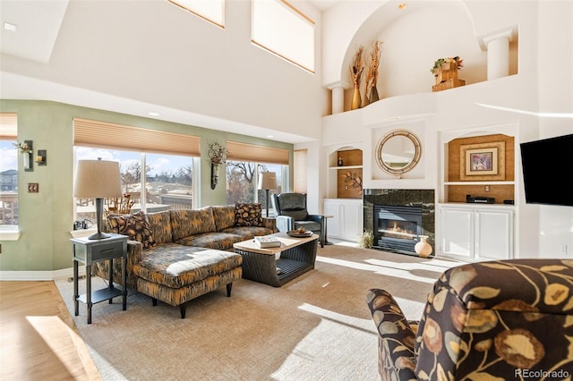 living room with a high ceiling, a premium fireplace, light wood-type flooring, and built in shelves