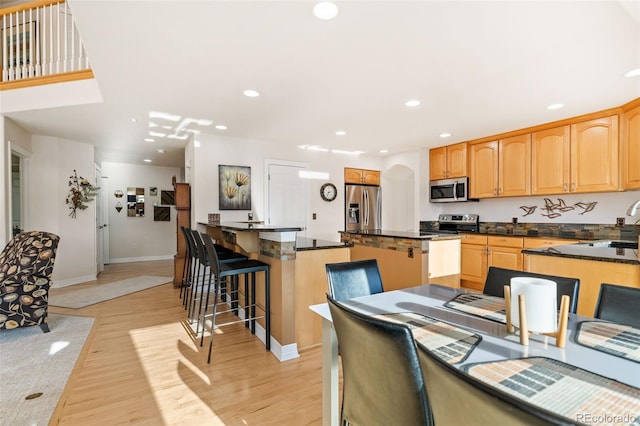 kitchen with stainless steel appliances, a center island, a kitchen breakfast bar, and light wood-type flooring