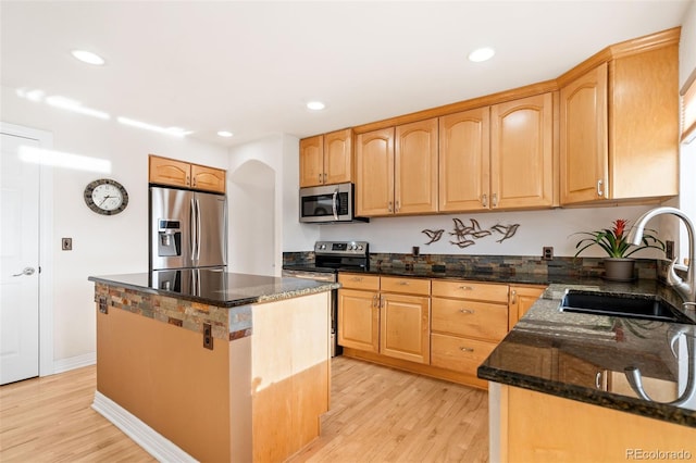 kitchen with appliances with stainless steel finishes, sink, dark stone counters, a center island, and light hardwood / wood-style flooring