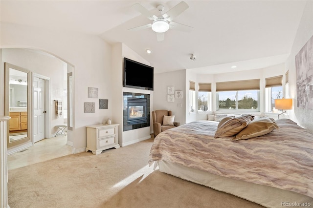 carpeted bedroom with a fireplace, vaulted ceiling, ceiling fan, and ensuite bathroom