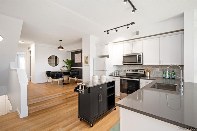 kitchen with sink, white cabinetry, a center island, hanging light fixtures, and appliances with stainless steel finishes