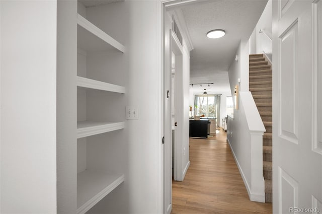 hall featuring track lighting, a textured ceiling, and light wood-type flooring