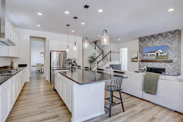 kitchen featuring decorative light fixtures, a kitchen bar, a kitchen island with sink, white cabinets, and a fireplace