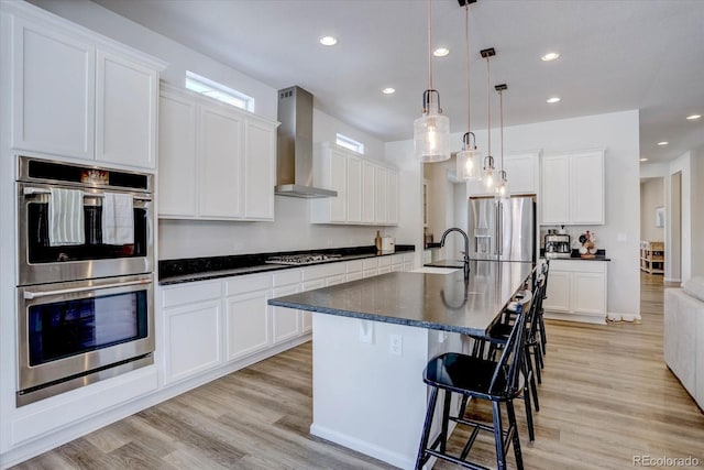 kitchen with decorative light fixtures, stainless steel appliances, wall chimney exhaust hood, and white cabinetry