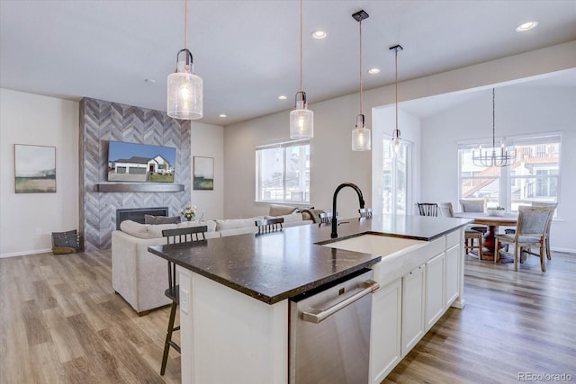 kitchen with stainless steel dishwasher, decorative light fixtures, an island with sink, a tile fireplace, and white cabinets