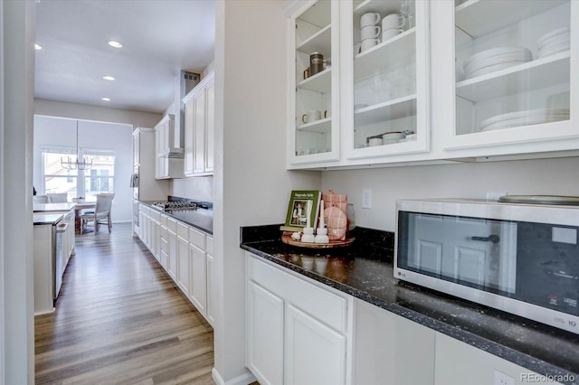 kitchen featuring stainless steel appliances, decorative light fixtures, white cabinetry, light hardwood / wood-style flooring, and dark stone counters