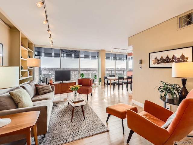 living area featuring floor to ceiling windows, track lighting, visible vents, and light wood-style floors