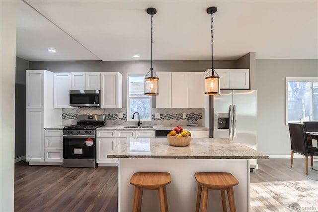 kitchen with stainless steel appliances, tasteful backsplash, a sink, and dark wood finished floors