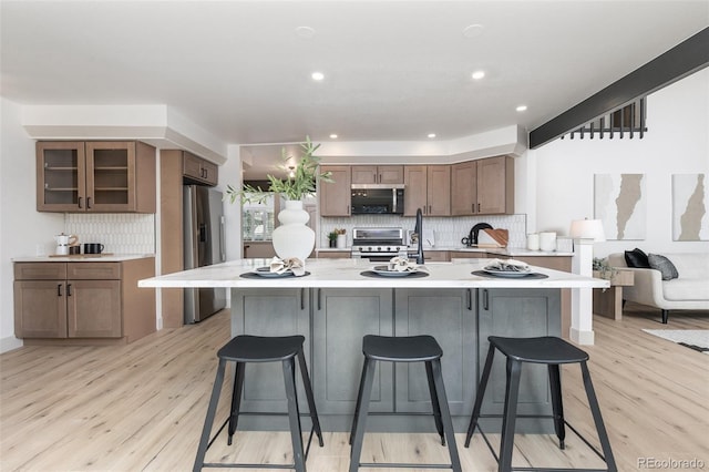 5814 Cole Way, Arvada, CO 80004 - kitchen featuring stainless steel appliances, light countertops, a breakfast bar area, decorative backsplash, and light wood-type flooring