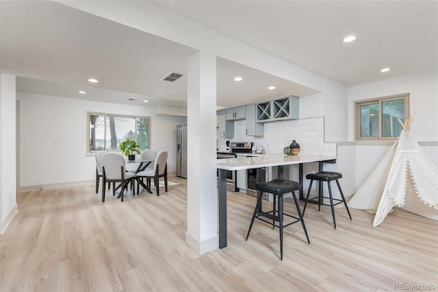5814 Cole Way, Arvada, CO 80004 - kitchen featuring appliances with stainless steel finishes, backsplash, light wood-style flooring, recessed lighting, and a kitchen bar