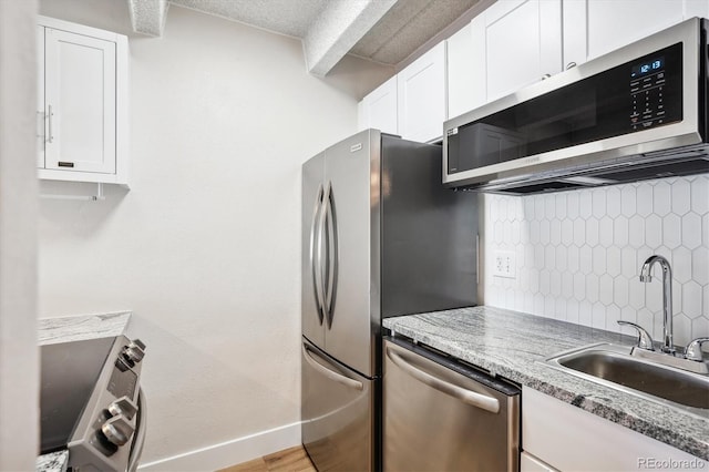 kitchen with backsplash, appliances with stainless steel finishes, white cabinetry, light stone countertops, and sink