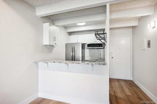 kitchen with appliances with stainless steel finishes, light wood-type flooring, a textured ceiling, kitchen peninsula, and white cabinets