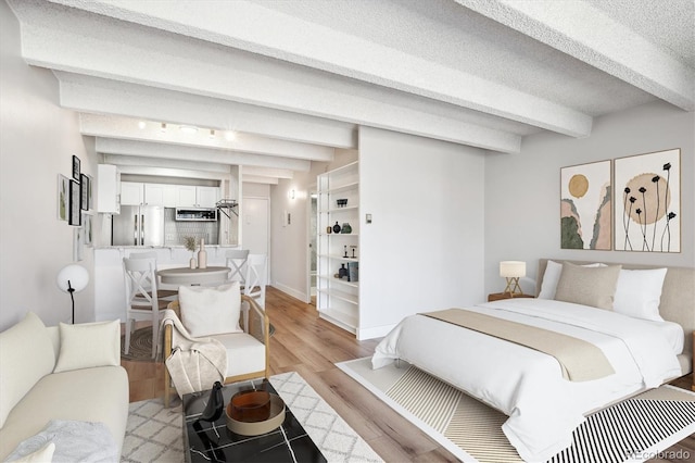 bedroom featuring light wood-type flooring, beamed ceiling, a textured ceiling, and stainless steel refrigerator