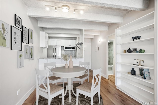 dining area with beam ceiling, hardwood / wood-style floors, track lighting, and a textured ceiling