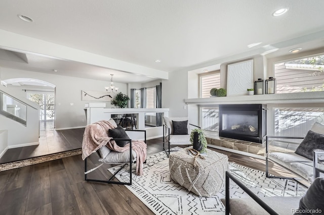 living area featuring a notable chandelier, a fireplace, arched walkways, hardwood / wood-style floors, and baseboards