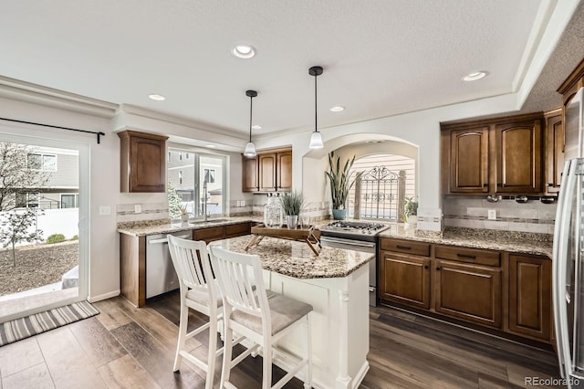 kitchen with appliances with stainless steel finishes, a center island, arched walkways, dark wood finished floors, and recessed lighting