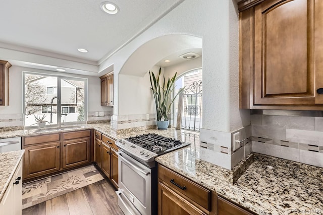 kitchen with appliances with stainless steel finishes, arched walkways, a sink, light stone counters, and light wood finished floors