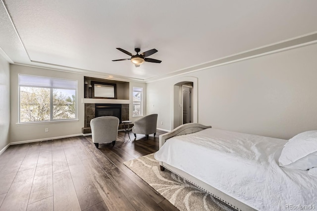 bedroom with arched walkways, baseboards, multiple windows, and a tile fireplace