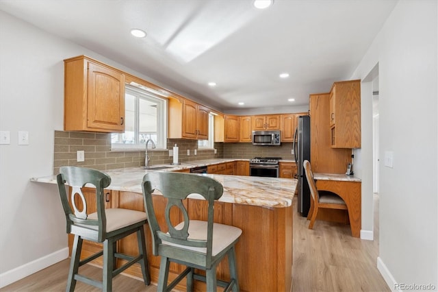 kitchen with a kitchen bar, kitchen peninsula, light wood-type flooring, and appliances with stainless steel finishes