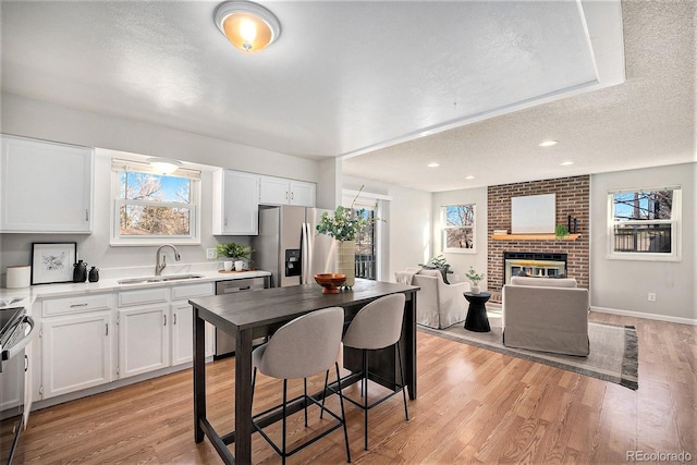 kitchen featuring appliances with stainless steel finishes, a fireplace, white cabinetry, sink, and light wood-type flooring