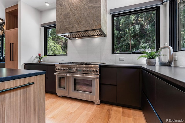 kitchen featuring decorative backsplash, light wood-type flooring, premium range hood, and range with two ovens