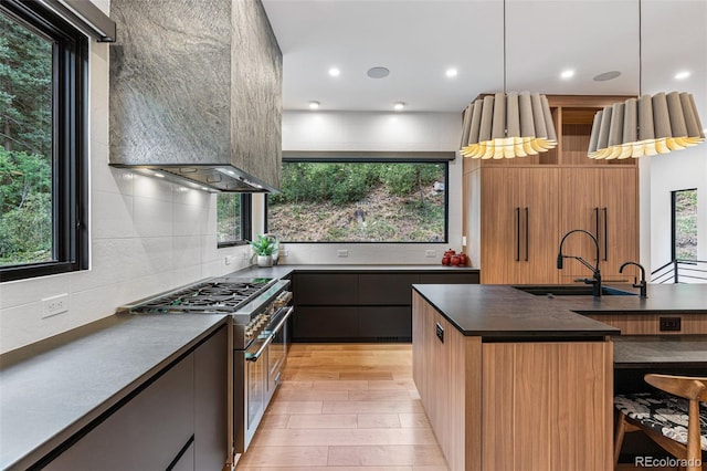 kitchen featuring light hardwood / wood-style floors, sink, hanging light fixtures, wall chimney range hood, and high end range