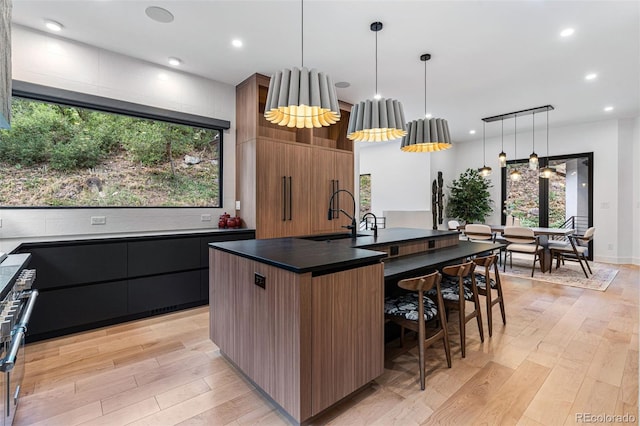 kitchen with light hardwood / wood-style flooring, a center island with sink, decorative light fixtures, and sink